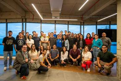 Educação Corporativa no Banco do Brasil – Fortalecendo Equipes com o CESAR Grupo de cerca de 30 profissionais sorridentes posa em escritório moderno com grandes janelas de vidro ao fundo.