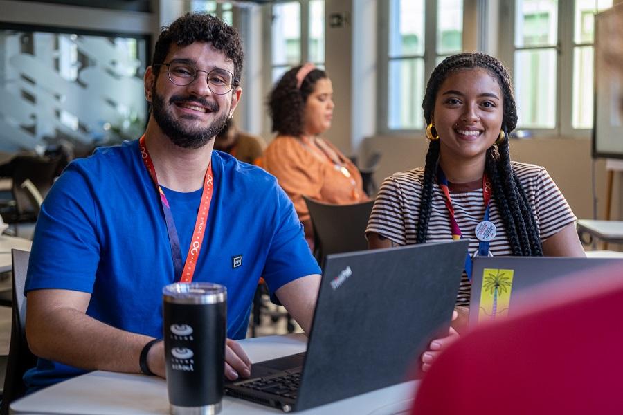 Alunos da C.E.S.A.R sorrindo para a câmera utilizando aparelhos notebook em espaço comum