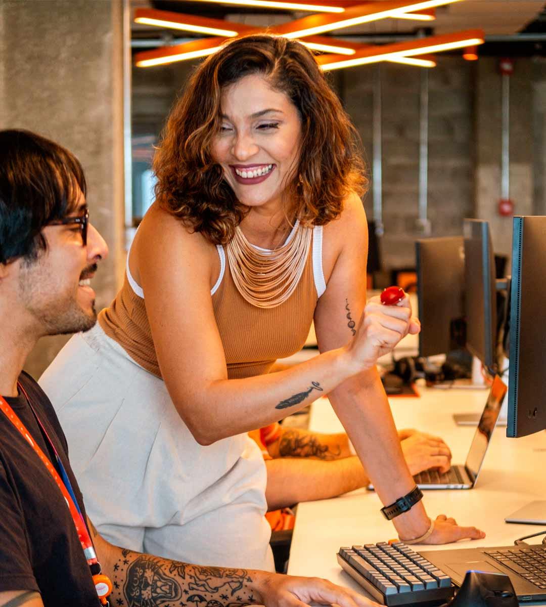 Duas pessoas sorrindo na frente de uma tela de computador