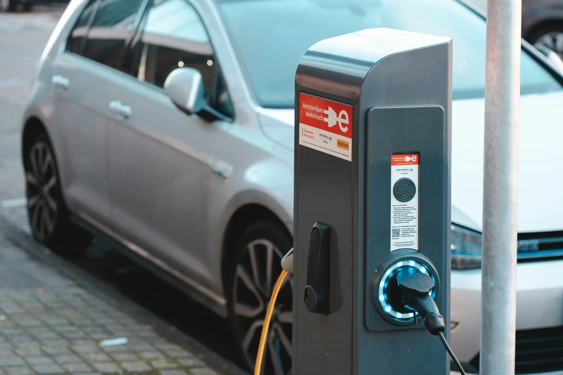 Carregamento de veículos elétricos e as novas tecnologias do setor Totem de carregamento de veículos elétricos com luz azul conectado a um carro prata estacionado na rua em Amsterdã.