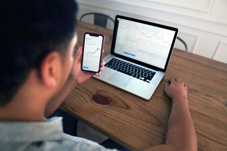 Análise de gráfico financeiro em dispositivos móveis Pessoa analisa gráficos financeiros em smartphone e notebook sobre mesa de madeira