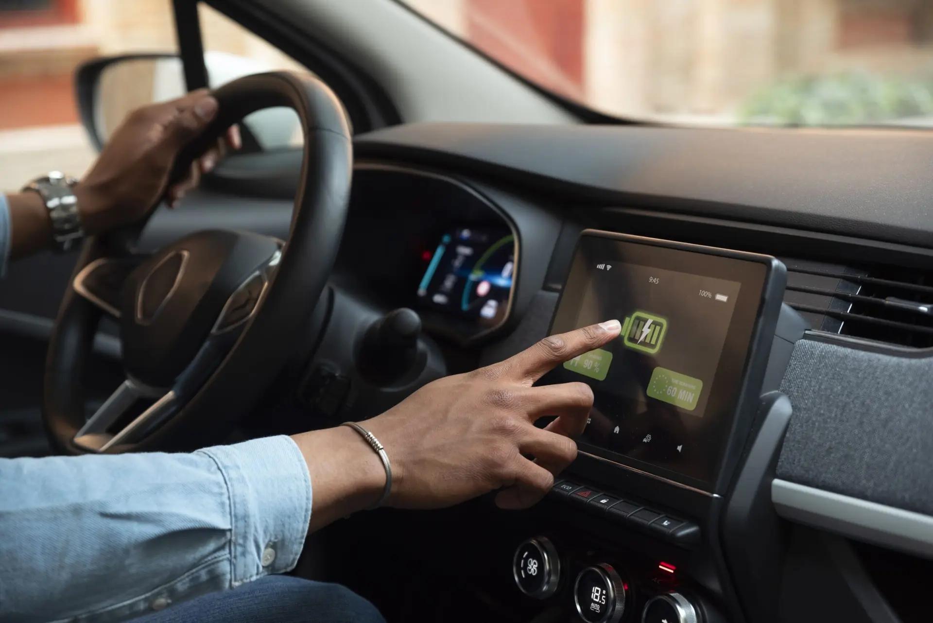 Veículos autônomos transformam a mobilidade do futuro Motorista toca em tela multimídia de carro elétrico que exibe o nível de carga da bateria e tempo de carregamento.