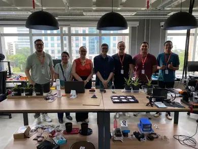 CBA transforma dados em sustentabilidade através do monitoramento do solo Sete profissionais posam atrás de bancadas com mudas de plantas e componentes eletrônicos num laboratório moderno