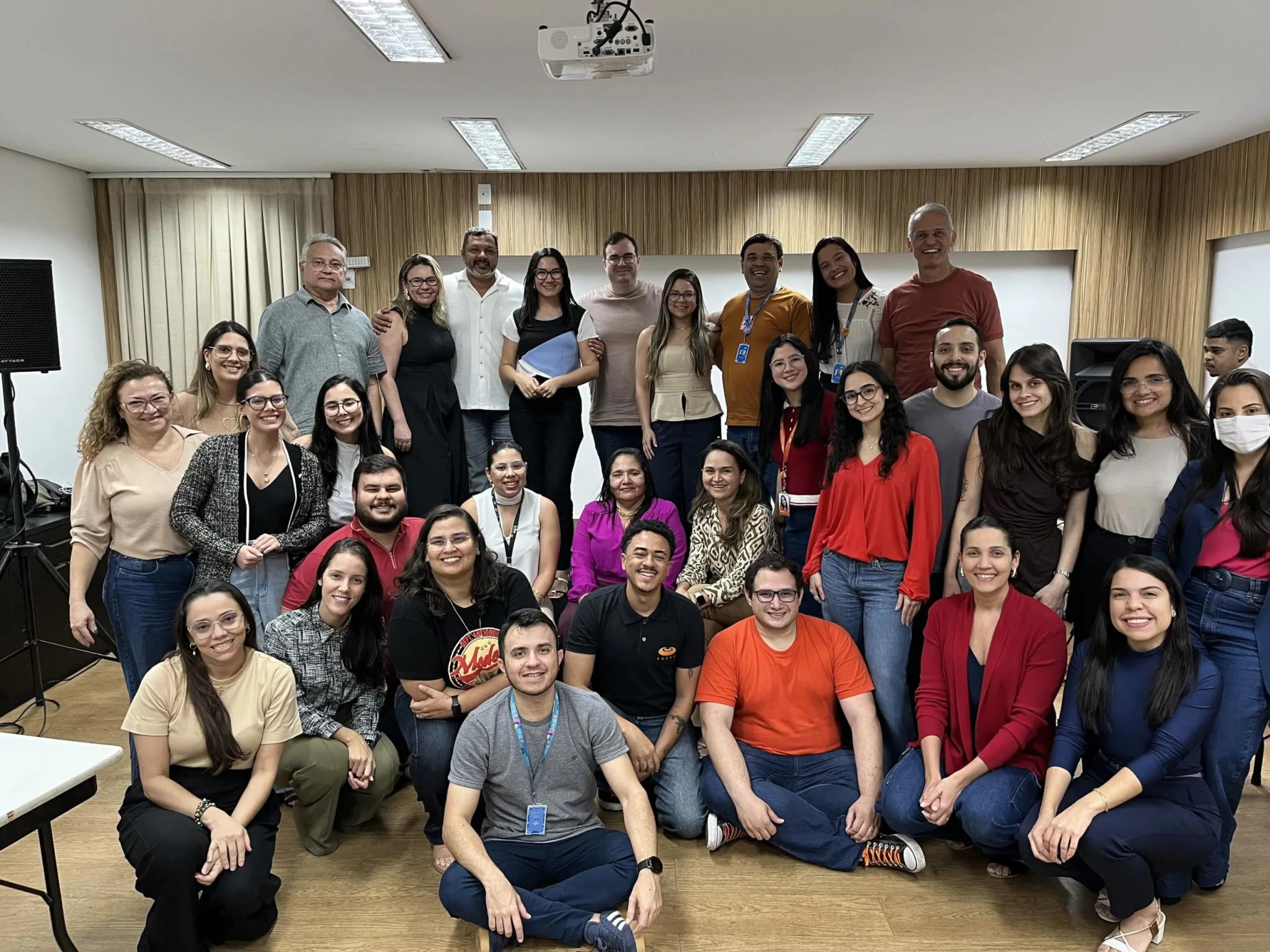 Sebrae RN e CESAR: Fortalecendo a cultura data-driven na educação corporativa Grupo de aproximadamente 30 profissionais sorrindo em uma sala de treinamento. Estão distribuídos em pé, sentados e agachados